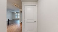 This single-floor residence offers a clean, modern aesthetic throughout, anchored by warm wood-look flooring that flows seamlessly from room to room. The open-concept kitchen serves as a central highlight, featuring dark espresso cabinetry, granite-style countertops, a peninsula with bar seating, and pendant lighting overhead. Black appliances complement the bold cabinetry, while a set of double doors provides convenient pantry or storage access nearby.

The living areas are bright and welcoming, with ceiling fans, multiple windows dressed with white blinds, and neutral wall tones that create a calm, versatile backdrop. Track lighting in the hallway adds a functional design touch as it connects the various living spaces.

The bathroom is well-equipped with a dual-sink vanity set in dark cabinetry topped with granite-look counters, a large framed mirror with Hollywood-style lighting, and a full soaking tub with tiled surround. Wood-look flooring extends into the bathroom for a cohesive feel.

A generously sized walk-in closet features multi-tiered wire shelving and hanging rods along multiple walls, offering ample organization potential. Throughout the space, two-panel interior doors with brushed nickel hardware provide a consistent and polished finishing touch.