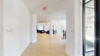 Located in Oakmont, PA, this single-floor amenity space offers a generously sized, thoughtfully designed environment spread across a substantial footprint. The interior is defined by a clean, modern aesthetic with crisp white walls, light-toned hardwood flooring, and bold white baseboard trim that unify the space throughout.

The centerpiece of the facility is a grand lounge area featuring a striking coffered ceiling with integrated ambient lighting, a classic white fireplace surround, large-scale flat-screen display, and floor-to-ceiling glass doors that frame outdoor greenery. Plush leather seating arrangements provide comfortable gathering zones within this elegant setting.

Adjacent to the lounge, a social lounge and kitchenette area includes high-top bistro tables with stylish seating, a full-size stainless steel refrigerator, and dark cabinetry — ideal for casual dining or entertaining. Smaller breakout rooms with natural light from full-height windows offer intimate seating for quiet conversation or small meetings.

The fitness center is a standout feature, divided into two well-equipped zones: a cardio room lined with treadmills, stationary bikes, and an elliptical alongside a bank of large windows, and a strength training room outfitted with cable machines, resistance equipment, spin bikes, and a wall-mounted television. Durable rubber flooring and recessed lighting complete this functional space.