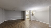 Located at 1110 Garden Walk Blvd in Atlanta, GA, this single-story, 3-bedroom, 2-bathroom home offers a functional and well-appointed layout. The open living room features rich hardwood-style flooring, neutral gray walls with classic chair-rail molding, and a textured ceiling, creating a clean and versatile living space. A pendant light fixture marks the transition into the adjacent kitchen-living area, which flows seamlessly into a fully equipped kitchen. The kitchen is outfitted with crisp white cabinetry, light speckled countertops, a double-basin stainless steel sink, a decorative tile backsplash in warm earth tones, and black appliances including a refrigerator and dishwasher. Both bathrooms are finished with wood-style flooring, white tub-shower combinations with chrome fixtures, and granite-style vanity countertops. The three bedrooms feature soft carpeting and large windows that invite natural light and outdoor views of surrounding greenery. A dedicated laundry area with utility hookups adds everyday convenience. Throughout the home, consistent neutral tones and clean finishes contribute to a cohesive, move-in-ready aesthetic.