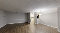Located at 1110 Garden Walk Blvd in Atlanta, GA, this single-story, 3-bedroom, 2-bathroom home offers a functional and well-appointed layout. The open living room features rich hardwood-style flooring, neutral gray walls with classic chair-rail molding, and a textured ceiling, creating a clean and versatile living space. A pendant light fixture marks the transition into the adjacent kitchen-living area, which flows seamlessly into a fully equipped kitchen. The kitchen is outfitted with crisp white cabinetry, light speckled countertops, a double-basin stainless steel sink, a decorative tile backsplash in warm earth tones, and black appliances including a refrigerator and dishwasher. Both bathrooms are finished with wood-style flooring, white tub-shower combinations with chrome fixtures, and granite-style vanity countertops. The three bedrooms feature soft carpeting and large windows that invite natural light and outdoor views of surrounding greenery. A dedicated laundry area with utility hookups adds everyday convenience. Throughout the home, consistent neutral tones and clean finishes contribute to a cohesive, move-in-ready aesthetic.