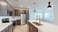 This well-appointed single-story home in McDonough, GA offers a thoughtfully designed layout with three bedrooms, two bathrooms, a dedicated laundry room, and two closets. The open-concept kitchen and living area serves as the heart of the home, where rich dark-stained cabinetry, stainless steel appliances — including a refrigerator, range, and microwave — and a large center island with a white quartz countertop and undermount sink create a functional and stylish cooking space. Pendant lighting and light hardwood flooring add warmth and character throughout. The living room is bright and airy, featuring multiple windows that invite abundant natural light and a ceiling fan for added comfort. The bedrooms are carpeted and generously sized, each with windows offering views of the surrounding neighborhood. The primary bedroom includes access to a walk-in closet with wire shelving. The bathrooms are finished with dark wood vanities, white countertops, and tile-surround tub-shower combinations. A dedicated in-unit laundry room accommodates a full-size washer and dryer. Clean white walls and consistent finishes throughout contribute to a cohesive, modern aesthetic that is both practical and inviting.