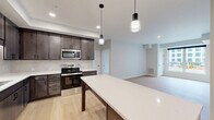 Located at 1310 Frost Ave in Maplewood, MN, this thoughtfully designed 2-bedroom, 1-bathroom single-floor residence offers a clean, modern aesthetic with high-quality finishes throughout. The open-concept kitchen and living area serves as the heart of the home, featuring dark-toned cabinetry, white quartz countertops, stainless steel appliances including a refrigerator, range, and built-in microwave, and a substantial center island with pendant lighting overhead. Light hardwood-style flooring flows throughout the main living areas, enhancing the bright and airy atmosphere. The living room receives natural light through large windows with views of the surrounding neighborhood. Both bedrooms are well-proportioned, with plush carpeting, individual windows that bring in natural light, and dedicated closet space — four closets in total across the unit. The shared full bathroom is finished with a dark wood vanity, dual sinks, white quartz countertops, framed mirrors with matte black hardware, and a tub-shower combination. A dedicated laundry area adds everyday convenience. The overall design palette — neutral walls, warm wood tones, and matte black accents — creates a cohesive, contemporary feel throughout the residence.
