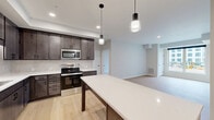 Located at 1310 Frost Ave in Maplewood, MN, this thoughtfully designed 2-bedroom, 1-bathroom single-floor residence offers a clean, modern aesthetic with high-quality finishes throughout. The open-concept kitchen and living area serves as the heart of the home, featuring dark-toned cabinetry, white quartz countertops, stainless steel appliances including a refrigerator, range, and built-in microwave, and a substantial center island with pendant lighting overhead. Light hardwood-style flooring flows throughout the main living areas, enhancing the bright and airy atmosphere. The living room receives natural light through large windows with views of the surrounding neighborhood. Both bedrooms are well-proportioned, with plush carpeting, individual windows that bring in natural light, and dedicated closet space — four closets in total across the unit. The shared full bathroom is finished with a dark wood vanity, dual sinks, white quartz countertops, framed mirrors with matte black hardware, and a tub-shower combination. A dedicated laundry area adds everyday convenience. The overall design palette — neutral walls, warm wood tones, and matte black accents — creates a cohesive, contemporary feel throughout the residence.