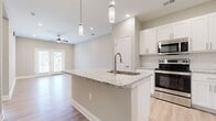 Located at 8000 Carlow Dr in Kernersville, NC, this well-appointed single-floor residence offers a thoughtfully designed open-concept layout. The combined kitchen and living area serves as the heart of the home, highlighted by a central island with a granite countertop and undermount sink, white shaker cabinetry, a classic subway tile backsplash, and a full suite of stainless steel appliances. Pendant lighting and recessed fixtures illuminate the space, while light hardwood-style flooring and neutral gray walls create a clean, modern aesthetic. The living area benefits from natural light through double French doors and is complemented by a ceiling fan. The spacious bedroom features plush carpeting, a generous window with outdoor views, and a ceiling fan. It connects to a walk-in closet outfitted with wire shelving for ample storage. The bathroom is finished with a double-sink vanity topped with granite, white cabinetry with brushed hardware, and tile flooring. A dedicated laundry room with wire shelving and utility connections adds everyday convenience. Throughout the residence, consistent neutral tones and quality finishes contribute to a cohesive and inviting atmosphere.