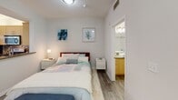 Located at 138 N Beaudry Ave in the heart of Los Angeles, this single-floor unit offers a thoughtfully designed open layout with a clean, modern aesthetic throughout. Wood-look flooring flows seamlessly from room to room, providing a cohesive and contemporary feel.

The kitchen is a standout feature, equipped with stainless steel appliances including a gas range, microwave, and refrigerator. Light wood cabinetry provides ample storage, while dark granite countertops and a multicolored mosaic tile backsplash add visual interest. A sliding door in the kitchen leads directly to a private outdoor balcony, allowing for natural light and outdoor access.

The sleeping area is positioned adjacent to the kitchen, separated by a half-wall peninsula that defines each zone while maintaining the open feel of the space. The bedroom area is bright and comfortable, with wall art and direct access to the bathroom. The bathroom features a vessel sink, wood-toned vanity, large wall mirror, and wood-look tile flooring.

The entry hallway is functional and well-organized, housing a closet alongside an in-unit stacked Whirlpool washer and dryer — a practical convenience. The living area receives natural light through multiple windows with horizontal blinds, creating a welcoming and airy atmosphere throughout the unit.