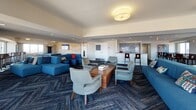 Located at 112 Somerset St in New Brunswick, NJ, this contemporary lounge space offers a well-appointed, single-floor layout designed for both socializing and relaxation. The space is characterized by a cohesive modern aesthetic, anchored by richly patterned herringbone-style carpeting in deep charcoal tones that runs throughout.

Multiple distinct seating areas provide versatile arrangements for gathering. Plush blue sectional sofas and mid-century-inspired upholstered armchairs are grouped around wooden coffee tables, creating comfortable conversation zones. A dedicated game area features a full-size pool table illuminated by a striking molecular-style chandelier with metallic globe pendants, adding a bold design focal point.

A wet bar with mosaic tile backsplash and bar stool seating is tucked along one wall, enhancing the space's entertainment functionality. Near the expansive windows, a high-top bistro table with swivel chairs offers a casual seating option with panoramic views of the New Brunswick skyline and surrounding landscape. Colorful abstract artwork adorns the walls throughout, complementing the upbeat, modern atmosphere. Recessed and flush-mount lighting ensures the space is well-lit, contributing to its inviting and energetic ambiance.