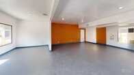 Located at 10860 N 85th Ave in Peoria, Arizona, this dedicated fitness center offers a well-equipped exercise space designed to support a wide range of workout routines. The room features a bold design aesthetic, highlighted by a striking orange textured accent wall that energizes the space, contrasted by clean white walls adorned with motivational fitness artwork. Blue baseboards add a finishing detail that ties the color scheme together throughout.

The durable gray concrete flooring provides a practical, low-maintenance surface suitable for high-traffic use. Large windows along multiple walls allow natural light to fill the room and offer views of the surrounding outdoor greenery, creating an open and inviting atmosphere. Recessed ceiling lighting supplements natural light, ensuring the space is well-lit at all times. A wall-mounted flat-screen television is positioned near the cardio area for entertainment during workouts.

Equipment is thoughtfully arranged throughout the room. The cardio zone includes multiple treadmills and an elliptical machine, while a multi-functional cable machine supports strength training. Free weight options include a full dumbbell rack with adjustable benches, along with stability balls and medicine balls stored on a dedicated wall-mounted rack. A large mirror panel reflects the space, enhancing the sense of openness. This fitness center is a comprehensive facility suited for both cardio and strength-focused training.