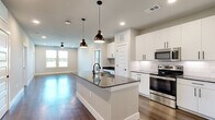 This well-appointed single-floor residence offers 2 bedrooms, 2 bathrooms, and 2 closets in a thoughtfully designed open layout. The kitchen and living area share a seamless open-concept space anchored by a large central island with dark granite countertops and an undermount sink, illuminated by stylish bronze pendant lights. White shaker-style cabinetry, a classic subway tile backsplash, and stainless steel appliances — including a range, microwave, and refrigerator — complete the kitchen. Rich hardwood flooring flows throughout the main living areas, complemented by neutral-toned walls and recessed lighting that create a bright, clean atmosphere. Natural light pours in through multiple windows. Both bedrooms feature plush carpet flooring and ceiling fans, with windows offering outdoor views. The primary bedroom is generously sized and connects to an en suite bathroom showcasing a double-sink vanity with dark granite countertops, backlit mirrors, white cabinetry with matte black hardware, hardwood floors, and a glass-enclosed shower. A well-organized walk-in closet with built-in shelving and hanging rods adds valuable storage. The second bathroom mirrors the same upscale finishes. The home's cohesive modern aesthetic, quality materials, and functional design make it a refined and comfortable living space.