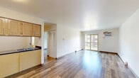 Located at 31 Olympic Village in Chicago Heights, IL, this one-bedroom, one-bathroom unit offers a practical and well-organized layout across a single floor. The open-plan living and dining area is a central highlight, featuring warm hardwood-style flooring that flows throughout the unit, bright white walls, and a sliding glass door that opens onto a private balcony, filling the space with natural light and providing outdoor views. The kitchen is efficiently designed with light wood cabinetry, dark countertops, a gas range, refrigerator, and a stainless steel sink — all positioned along one wall for a clean, functional workspace. The spacious bedroom offers generous storage with two louvered bi-fold closets spanning nearly an entire wall, complemented by a window that brings in additional natural light. The bathroom includes a wood-vanity with a large mirror, a tiled shower-tub combination, built-in shelving, and hardwood-style flooring. Baseboard heating is present throughout the unit, and a wall-mounted air conditioning unit serves the living area. The overall ambiance is clean, neutral, and move-in ready, suited for comfortable everyday living.