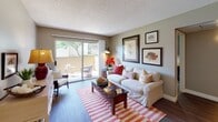 This single-floor model unit at 11355 Zapata in San Diego presents a well-organized layout with a cohesive nautical design theme carried throughout. The living room serves as the central gathering space, featuring hardwood-style flooring, a textured ceiling, and a large sliding glass door that opens to a private patio with outdoor seating and tree-lined views, filling the room with natural light. Framed coastal artwork adorns the walls, complementing the relaxed aesthetic.

Adjacent to the living room, the dining area accommodates a round table with wicker chairs beneath a multi-bulb ceiling fixture, and connects directly to the kitchen. The kitchen is equipped with white cabinetry, a double stainless steel sink, laminate countertops, a stainless dishwasher, and a full-size refrigerator.

The primary bedroom is generously sized with carpet flooring, a window offering outdoor views, and nautical wall art. A secondary bedroom provides similar comfort with carpet, a window, closet access, and space for a desk and bed. Two bathrooms serve the unit, each with wood-style flooring, vanity storage, and tasteful coastal décor. The overall ambiance is bright, cohesive, and functional.