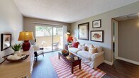 This single-floor model unit at 11355 Zapata in San Diego presents a well-organized layout with a cohesive nautical design theme carried throughout. The living room serves as the central gathering space, featuring hardwood-style flooring, a textured ceiling, and a large sliding glass door that opens to a private patio with outdoor seating and tree-lined views, filling the room with natural light. Framed coastal artwork adorns the walls, complementing the relaxed aesthetic.

Adjacent to the living room, the dining area accommodates a round table with wicker chairs beneath a multi-bulb ceiling fixture, and connects directly to the kitchen. The kitchen is equipped with white cabinetry, a double stainless steel sink, laminate countertops, a stainless dishwasher, and a full-size refrigerator.

The primary bedroom is generously sized with carpet flooring, a window offering outdoor views, and nautical wall art. A secondary bedroom provides similar comfort with carpet, a window, closet access, and space for a desk and bed. Two bathrooms serve the unit, each with wood-style flooring, vanity storage, and tasteful coastal décor. The overall ambiance is bright, cohesive, and functional.