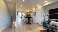 This two-floor residence offers a thoughtfully designed layout that balances style and functionality throughout. The main level showcases an open-concept living and kitchen area anchored by light-toned luxury vinyl plank flooring that runs seamlessly through the space. The kitchen is equipped with stainless steel appliances, a tile backsplash in a geometric pattern, ample soft-gray cabinetry with clean-line hardware, and light quartz countertops. A central high-top bar table with bar stools provides a casual dining option, while a dedicated peninsula with counter seating adds additional workspace. Recessed lighting and pendant fixtures illuminate the kitchen and living areas, complemented by natural light from a sliding glass door at the rear. The living room is a comfortable gathering space featuring dual windows, a ceiling fan, and hardwood-style flooring. Upstairs, the bedrooms are carpeted and bathed in natural light through large windows with outdoor views of surrounding greenery. The bathroom includes a soaking tub with clean white tile surround and a decorative mosaic accent border. A dedicated laundry area with stacked washer and dryer units adds everyday convenience. Neutral warm tones and modern finishes are carried consistently throughout, creating a cohesive and welcoming ambiance across both floors.