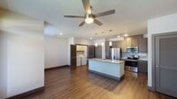 This single-story unit in Houston, TX offers a well-designed open-concept layout that seamlessly connects the living, dining, and kitchen areas. The kitchen serves as the centerpiece of the space, featuring a large granite-topped island with an undermount sink, sleek dark-toned cabinetry extending to the ceiling, stainless steel appliances including a French door refrigerator, range, and microwave, and a tile backsplash. Pendant lighting and a track light fixture illuminate the workspace effectively.

The living area is finished with warm wood-look plank flooring and is topped by a ceiling fan, while a front entry door with a transom window allows natural light into the space. The bedroom offers plush carpeting, a ceiling fan, and a window with blinds. The bathroom includes a granite-topped vanity with dark cabinetry, a tub/shower combination with tiled surround, and access to a walk-in closet. A dedicated laundry area with side-by-side washer and dryer connections is conveniently tucked within the unit. Throughout, neutral walls and consistent dark trim create a cohesive, modern aesthetic.