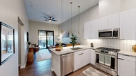 Located in Scottsdale, Arizona, this thoughtfully designed one-bedroom, one-bathroom residence offers a modern aesthetic with high-end finishes throughout. Soaring ceilings amplify the sense of space across the open-concept floor plan, while wood-style flooring flows seamlessly from room to room.

The kitchen is a standout feature, boasting crisp white cabinetry, a white subway tile backsplash, stainless steel appliances including a gas range, microwave, dishwasher, and refrigerator, and a peninsula with a quartz countertop that provides bar seating beneath stylish pendant lighting. The kitchen opens directly to the living room, creating an ideal space for entertaining.

The living room is bright and welcoming, with soaring walls and large black-framed sliding glass doors that lead to a private patio, bringing in abundant natural light and outdoor views of the surrounding Scottsdale landscape.

The generously sized bedroom features tall ceilings, a window with views of lush desert greenery, and warm, neutral tones that create a calm retreat. The bathroom is finished with a white floating vanity, quartz countertop, black matte hardware, a large wood-framed mirror, and a walk-in glass-enclosed shower with tile surround. A hallway connects the living spaces with practicality and ease.