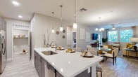 This thoughtfully designed single-floor residence offers a seamless blend of modern finishes and functional living spaces throughout. The open-concept kitchen serves as the heart of the home, anchored by a large quartz waterfall island with an undermount sink and seating for multiple guests. Dark wood cabinetry, a tile backsplash, stainless steel appliances, and elegant pendant lighting complete the space, which flows directly into a combined dining and living area. The living room is bright and welcoming, featuring large windows that invite natural light and views of surrounding greenery, complemented by a ceiling fan and direct access to an outdoor area. Two bedrooms provide comfortable retreats, each with plush carpeting, ceiling fans, and generous natural light. The primary bedroom connects to a well-appointed en-suite bathroom featuring a dual-sink vanity with dark wood cabinetry, a glass-enclosed shower, wood-look tile flooring, and direct access to a spacious walk-in closet with multi-tier shelving. A second full bathroom offers a tub-shower combination and additional storage cabinetry. A dedicated in-unit laundry room with stacked washer and dryer rounds out this well-equipped residence, delivering convenience and comfort throughout.