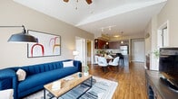 Located at 1501 NW 38th St in Kansas City, Missouri, this single-floor residence offers a thoughtfully designed open-concept layout that connects the living, dining, and kitchen areas seamlessly. The living room features vaulted ceilings with a ceiling fan, warm hardwood-style flooring, large windows that invite abundant natural light, and a neutral color palette that creates a welcoming ambiance throughout.

The kitchen is well-equipped with rich dark-wood cabinetry, stainless steel appliances including a range, microwave, and refrigerator, granite-style countertops, a classic white tile backsplash, and pendant lighting overhead. It opens directly to the dining area, making it ideal for entertaining.

The primary bedroom is a comfortable retreat with plush carpeting, a tray ceiling, and a window providing natural light. It offers direct access to both a walk-in closet outfitted with wire shelving systems and a private en-suite bathroom. The bathroom features tile flooring, a granite-topped vanity with dark wood cabinetry, and a full soaking tub and shower combination. An additional flexible room with large windows and carpeted flooring provides versatile living space. The overall design balances modern finishes with a warm, livable aesthetic.