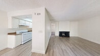 Located at 1000 Dumont Blvd in Las Vegas, Nevada, this single-floor, one-bedroom, one-bathroom unit offers a practical and well-organized layout. Light-toned vinyl plank flooring runs throughout the main living areas, complementing the clean white walls and creating a bright, cohesive aesthetic. The kitchen is efficiently designed with white cabinetry, wood-toned countertops, a full suite of white appliances including a gas range, dishwasher, and refrigerator, and a recessed ceiling with built-in lighting. It opens directly to the living room, which features a classic brick fireplace with a black surround and a textured ceiling, adding warmth and character to the space. The bedroom is generously proportioned, featuring rich dark hardwood-style flooring, a large window that brings in natural light and views of the surrounding exterior, and access to a spacious walk-in closet outfitted with dual shelving units on both sides. The bathroom includes an extended vanity with a stone-finish countertop, dual mirrors, and a full soaking tub with a shower. Clean white walls throughout maintain a neutral, move-in-ready atmosphere well-suited for comfortable everyday living in the heart of Las Vegas.