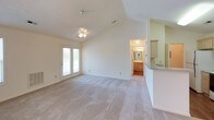 This single-story, 2-bedroom, 2-bathroom home offers a thoughtfully designed layout with a blend of comfort and functionality. The living area is a standout space, featuring dramatic vaulted ceilings that create an airy, open atmosphere. A ceiling fan with a light fixture is centrally positioned, and natural light filters in through a window, enhancing the sense of spaciousness. Soft carpet underfoot adds warmth to the living area. French doors provide a seamless connection to the outdoors, while a partial wall with a countertop separates the space from the kitchen. The galley-style kitchen is efficiently laid out with light wood cabinetry, a tile countertop, and white appliances, including a range and refrigerator. Hardwood-style flooring runs through the kitchen, adding a clean, practical finish. Both bedrooms are carpeted and receive natural light through windows. One bedroom includes a walk-in closet with built-in shelving, offering ample storage. The two full bathrooms are each equipped with a single-sink vanity with wood cabinetry, a tub-shower combination, and hardwood-style flooring, presenting a clean and functional design throughout.