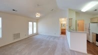 This single-story, 2-bedroom, 2-bathroom home offers a thoughtfully designed layout with a blend of comfort and functionality. The living area is a standout space, featuring dramatic vaulted ceilings that create an airy, open atmosphere. A ceiling fan with a light fixture is centrally positioned, and natural light filters in through a window, enhancing the sense of spaciousness. Soft carpet underfoot adds warmth to the living area. French doors provide a seamless connection to the outdoors, while a partial wall with a countertop separates the space from the kitchen. The galley-style kitchen is efficiently laid out with light wood cabinetry, a tile countertop, and white appliances, including a range and refrigerator. Hardwood-style flooring runs through the kitchen, adding a clean, practical finish. Both bedrooms are carpeted and receive natural light through windows. One bedroom includes a walk-in closet with built-in shelving, offering ample storage. The two full bathrooms are each equipped with a single-sink vanity with wood cabinetry, a tub-shower combination, and hardwood-style flooring, presenting a clean and functional design throughout.
