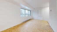 Located at 500 Avenue des Pins Ouest in the heart of Montréal, this studio offers a thoughtfully organized layout across a single floor. The main living area is bright and open, featuring warm parquet flooring in a classic basket-weave pattern and crisp white walls that create a clean, airy atmosphere. A large window frames city views, allowing natural light to fill the space and providing a pleasant urban backdrop.

The kitchen is a distinct, self-contained area finished with white cabinetry, white tile flooring, and full-sized appliances including a refrigerator and electric stove. A small window in the kitchen adds additional ventilation and light. The transition between the kitchen and living area is clearly defined by the change in flooring material.

The bathroom is well-appointed with a full-sized bathtub and tiled surround, a vanity with an integrated sink and mirror cabinet, and a charming mosaic tile floor with subtle yellow accents. A hallway connects the various areas and features a built-in closet with mirrored sliding doors, enhancing the sense of space. The entry door opens directly into this corridor, providing a functional transition zone. Overall, the studio presents a practical and tidy living environment suited for city life in Montréal.