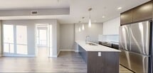 The View is a thoughtfully designed 2-bedroom, 2-bathroom residence that blends contemporary finishes with an open, functional layout. Light-toned hardwood flooring runs throughout the unit, creating a seamless flow from room to room.

The kitchen and living area form the heart of the home. The kitchen is anchored by a central island topped with striking veined quartz countertops and fitted with an undermount sink and sleek pendant lighting overhead. Dark wood cabinetry is paired with white upper cabinets and a full suite of stainless steel appliances, including a refrigerator, dishwasher, and range. The adjoining living area is bathed in natural light from expansive floor-to-ceiling windows that frame breathtaking city skyline views, giving the space an airy, elevated feel.

A clean, well-lit hallway connects the main living area to the private rooms and bathrooms. Both bathrooms exhibit a refined, spa-inspired aesthetic with marble-patterned tile on the floors and walls. One bathroom features a soaking tub with a tub surround, while the second offers a glass-enclosed walk-in shower. Both are equipped with floating dark wood vanities, white quartz countertops, undermount sinks, and large mirrors.

Recessed lighting and a neutral color palette throughout contribute to the space's bright, modern ambiance.