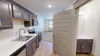 Located at 6313 Clinton Hwy in Knoxville, Tennessee, this single-floor unit offers a clean, modern layout designed for comfortable everyday living. The kitchen is a standout feature, equipped with rich dark wood cabinetry, light quartz-style countertops, a subway tile backsplash, and stainless steel appliances including a refrigerator, electric range with over-the-range microwave, and a deep single-basin sink with a contemporary brushed nickel faucet. Light wood-tone flooring runs throughout the kitchen and entryway, creating a warm and cohesive aesthetic. The living area transitions seamlessly from the kitchen and is finished with plush wall-to-wall carpet, offering a cozy atmosphere. A ceiling fan with a light fixture and a wall-mounted HVAC unit provide year-round climate control, while a window allows natural light to fill the space. The bedroom is generously proportioned, featuring the same soft carpeting, a ceiling fan, and a closet accessible through a paneled door. The bathroom is thoughtfully appointed with a full soaking tub and shower combo, accented by classic white subway tile and brushed nickel hardware, lending a crisp, timeless finish to the space.