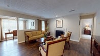 This model one-bedroom, one-bathroom residence at Belmont Crossing in Riverdale, Georgia presents a thoughtfully arranged single-story floor plan that balances functionality with comfortable living. The spacious living room serves as the heart of the home, featuring rich hardwood-style flooring, a textured ceiling, recessed lighting, and a tile-surround fireplace that anchors the room as a focal point. Multiple windows dressed with warm drapery allow natural light to fill the space, creating an inviting ambiance. Seating areas are generously sized, offering room for both relaxed lounging and entertaining.

Adjacent to the living area, a dedicated dining space accommodates a full dining set, ideal for everyday meals. The kitchen is equipped with rich wood cabinetry offering ample storage, a double-basin stainless steel sink, a dishwasher, and white appliances set against clean countertops.

The bedroom provides a calm retreat with carpeted flooring, a textured ceiling, and sufficient space for a full furniture arrangement. The bathroom includes a tub-shower combination with a curtain enclosure and hardwood-style flooring. A dedicated laundry area houses a full-size washer and dryer with overhead shelving for added storage convenience.