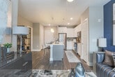 Located at 2565 Circle 75 Pkwy SE in Atlanta, Georgia, this single-floor residence offers a thoughtfully designed open-concept layout finished with contemporary details throughout. Dark hardwood-style flooring flows consistently across the living spaces, anchoring the modern aesthetic.

The kitchen serves as a central focal point, featuring white shaker cabinetry extending to the ceiling, a neutral tile backsplash, and a full suite of stainless steel appliances including a refrigerator, range, and built-in microwave. A large island with a light quartz countertop provides an integrated sink and bar-style seating beneath a set of bold square pendant lights, making it ideal for both meal preparation and casual dining.

The living area is bright and open, with floor-to-ceiling windows and a glass-paneled door leading to a private balcony, inviting generous natural light. The bedroom is a well-proportioned retreat featuring a ceiling fan, large windows with exterior views, and a dedicated dressing area with ample storage.

The bathroom is cleanly finished with white vanity cabinetry and a shower-tub combination. A dedicated laundry closet houses a stacked full-size washer and dryer, adding everyday convenience to this well-appointed space.