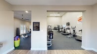 This fitness center in Hattiesburg, Mississippi offers a comprehensive workout facility spread across a single floor with multiple interconnected exercise zones. The space is characterized by soaring ceilings, neutral-toned walls, and durable rubber flooring throughout the workout areas, creating a clean and functional environment.

The main workout area is generously sized and lined with large mirrors, enhancing the sense of openness while allowing users to monitor their form. It is outfitted with a variety of cardio equipment, including multiple treadmills, elliptical trainers, and a rowing machine, as well as a recumbent bike. Strength training is well-represented with cable and weight machines, a dumbbell rack, stability balls, and benches.

Natural light fills the space through multiple sets of elegant French doors, which also provide direct outdoor access. Ceiling fans help maintain a comfortable atmosphere throughout. A wall-mounted flat-screen television is available in one of the cardio zones. Colorful fitness-themed artwork adorns the walls, adding visual energy to the space.

The entry area features light hardwood-style flooring, a water fountain, and restroom access, providing a welcoming transition into the facility. Posted fitness center rules ensure a safe and organized environment for all users.