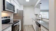 This thoughtfully designed two-bedroom, two-bathroom residence in Farmington Hills, Michigan, offers a comfortable and functional single-floor layout. The open-concept living and dining area features plush wall-to-wall carpeting, a ceiling fan, and a large sliding glass door that invites natural light and provides access to the outdoors. The kitchen is a standout feature, designed in a galley style with crisp white cabinetry, granite countertops, a subway tile backsplash, and a full suite of stainless steel appliances including a refrigerator, range, microwave, and dishwasher. A breakfast bar connects the kitchen to the living area, enhancing the open flow of the space. Light wood-style flooring runs throughout the kitchen, complementing the clean, modern aesthetic. Both bedrooms are generously sized with soft carpeting and windows that allow for ample natural light. The bathrooms are clean and well-appointed, featuring a soaking tub with tiled surround. A dedicated laundry area with a full-size washer and dryer adds everyday convenience. With neutral tones throughout and a practical, well-organized floor plan, this residence offers a polished and move-in-ready living experience.