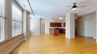 This single-floor space is defined by warm hardwood flooring that runs continuously throughout, creating a cohesive and inviting atmosphere. The open-concept living and kitchen area forms the heart of the unit, offering generous space bathed in natural light from multiple windows fitted with horizontal blinds. A ceiling fan overhead enhances comfort in the living zone.

The kitchen is well-appointed with rich cherry-toned cabinetry, dark granite countertops, stainless steel appliances including a range, microwave, and refrigerator, and a central island with a sink—ideal for both cooking and casual dining. A wine rack built into the upper cabinetry adds a distinctive touch.

Multiple bedrooms feature hardwood floors, large windows with urban views, and ample natural light. The primary bedroom stands out with a stylish barn door leading to a built-in shelving closet, dual windows, and a ceiling fan. Additional bedrooms offer dedicated closet space with sliding panel doors and wire shelving. The bathroom includes a glass-enclosed corner shower with tile surround, a cherry-toned vanity, and dark granite countertops, maintaining the consistent material palette found throughout the space.