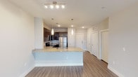 Located in Mansfield, TX, this single-floor residence presents a clean, contemporary design with a well-thought-out open-concept layout. The kitchen serves as a central highlight, showcasing dark espresso cabinetry paired with granite countertops, a stainless steel refrigerator, range, and microwave. A peninsula island with an undermount sink and pendant lighting overhead defines the boundary between the kitchen and the living area, creating a natural flow between the two spaces.

The living area features wood-style plank flooring and a ceiling fan with integrated lighting, complemented by track lighting for additional illumination. Neutral-toned walls throughout the unit lend a bright, airy atmosphere. A hallway corridor leads to multiple doors, providing organized access to bedrooms and additional rooms.

The bedroom is carpeted for comfort, with natural light entering through double windows fitted with blinds and a ceiling fan above. The bathroom is finished with matching granite countertops, dark cabinetry, a framed mirror with wall sconce lighting, and wood-style flooring that carries the cohesive aesthetic found throughout the unit. A window at the end of the bathroom hallway adds natural light to the space.
