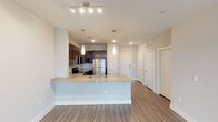 Located in Mansfield, TX, this single-floor residence presents a clean, contemporary design with a well-thought-out open-concept layout. The kitchen serves as a central highlight, showcasing dark espresso cabinetry paired with granite countertops, a stainless steel refrigerator, range, and microwave. A peninsula island with an undermount sink and pendant lighting overhead defines the boundary between the kitchen and the living area, creating a natural flow between the two spaces.

The living area features wood-style plank flooring and a ceiling fan with integrated lighting, complemented by track lighting for additional illumination. Neutral-toned walls throughout the unit lend a bright, airy atmosphere. A hallway corridor leads to multiple doors, providing organized access to bedrooms and additional rooms.

The bedroom is carpeted for comfort, with natural light entering through double windows fitted with blinds and a ceiling fan above. The bathroom is finished with matching granite countertops, dark cabinetry, a framed mirror with wall sconce lighting, and wood-style flooring that carries the cohesive aesthetic found throughout the unit. A window at the end of the bathroom hallway adds natural light to the space.