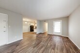 This single-floor residence in East Ridge, Tennessee offers a practical and well-organized layout designed for comfortable living. The open living area greets you upon entry, showcasing rich, dark wood-look vinyl flooring, neutral gray walls, and a textured ceiling that carries throughout much of the home. A light-filled entry door with a paneled window brings in natural light, creating a bright and welcoming atmosphere.

The kitchen is positioned adjacent to the living space in an open, semi-connected layout. It features white cabinetry, dark countertops, a black refrigerator, and a stainless steel sink, providing a clean and functional workspace. A peninsula-style counter separates the kitchen from the living area, enhancing the sense of flow between spaces.

The bedrooms are carpeted with a neutral, soft-toned carpet and include closet storage. One bedroom features a window overlooking greenery, adding a touch of natural scenery. A hallway connects the sleeping areas to a bathroom equipped with white cabinetry, a dark countertop vanity, a medicine cabinet mirror, and wood-look flooring.

Additional areas visible from the layout include a secondary living or flex space and a corridor leading to private rooms. Throughout the home, consistent neutral tones, clean finishes, and functional design elements create a cohesive and move-in-ready environment.