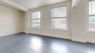 Located on the seventh floor of a building in the heart of downtown Jacksonville, this one-bedroom, two-bathroom apartment offers an efficient and well-organized layout. The open-concept living and kitchen area forms the core of the space, featuring smooth gray epoxy-style flooring that extends throughout the main living areas. The kitchen is equipped with warm wood cabinetry, black appliances including a refrigerator and built-in microwave, and a peninsula with a built-in sink that provides both additional prep space and a natural division from the living area. The living room benefits from multiple large windows fitted with horizontal blinds, allowing generous natural light and framing elevated views of the surrounding downtown cityscape. A ceiling fan adds a practical touch overhead. The bedroom continues the bright, neutral palette with light-toned tile flooring and multiple windows offering sweeping views of Jacksonville's urban skyline. Two full bathrooms complete the unit, each featuring a tub-shower combination with white tile surround, a vanity with warm wood cabinetry, and the same consistent gray flooring. A dedicated closet provides additional storage. The overall aesthetic is clean, minimal, and functional, making this a well-suited urban residence in the vibrant core of downtown Jacksonville.