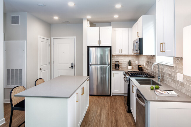 Design Collection II (South Building) Kitchen with white cabinetry, gold pulls, beige tile backsplash, grey quartz countertops, stainless steel appliances, and hard surface flooring - Avalon Somerville Station