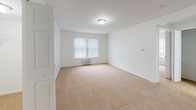 This single-floor residential unit offers a practical and well-organized layout designed for comfortable everyday living. The living area is spacious and open, featuring warm beige carpeting and crisp white walls that create a bright, neutral atmosphere. A pass-through window connects the living space to the kitchen, enhancing the sense of openness and allowing easy communication between rooms. The galley-style kitchen is efficiently designed with white cabinetry, dark countertops, a double-basin sink, and wood-look flooring. A window at the end of the kitchen allows natural light to filter in, keeping the space feeling airy. Two carpeted bedrooms provide comfortable private retreats, each featuring large windows with vertical blinds that allow natural light while maintaining privacy. One bedroom includes a wall-mounted air conditioning unit for individual climate control. The full bathroom is finished in white with a vanity featuring dark countertops and white cabinetry, a combined shower and bathtub, and bright overhead lighting. Adjacent to the bathroom is a linen closet with built-in shelving, offering convenient storage. Throughout the unit, consistent white walls, neutral flooring choices, and clean finishes contribute to a cohesive, move-in-ready aesthetic.