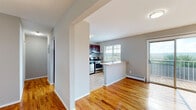 This single-floor unit offers a well-designed layout that balances comfort and functionality throughout. Warm-toned hardwood flooring flows consistently across the living areas and bedrooms, contributing to a cohesive and inviting ambiance. The kitchen is equipped with rich dark wood cabinetry, stainless steel appliances including a gas range and refrigerator, a double sink, and light countertops. A peninsula breakfast bar connects the kitchen to the main living area, creating an open and social feel. A large window in the kitchen frames scenic views of the surrounding landscape, filling the space with natural light. The living area is generously proportioned and opens directly to a private balcony through sliding glass doors, offering sweeping outdoor views of the tree-lined surroundings. The bedrooms are well-sized, finished with the same hardwood flooring, and include closets with built-in shelving for ample storage. Each room is served by baseboard heating, and select rooms include wall-mounted air conditioning units. Neutral gray walls throughout provide a clean, modern backdrop. The overall layout, as seen in the dollhouse view, is efficient and open, making excellent use of the available space across all areas.