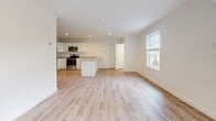 This thoughtfully designed single-floor unit offers a clean, contemporary aesthetic throughout, characterized by crisp white walls, light-toned luxury vinyl plank flooring in the main living areas, and an abundance of natural light from multiple windows. The open-concept layout seamlessly connects the kitchen and living space, creating a generous and airy atmosphere ideal for everyday living and entertaining. Sliding glass doors in the living area provide direct access to the outdoors and invite views of the surrounding greenery. The kitchen is well-appointed with white shaker-style cabinetry, light stone countertops, a central island with shiplap detailing, and a full suite of stainless steel appliances including a refrigerator, range, microwave, and dishwasher. Two bedrooms feature plush wall-to-wall carpeting and operable windows that frame views of the landscaped exterior. Each bedroom is equipped with a wall-mounted mini-split unit and baseboard heating for year-round climate control. The full bathroom is finished with light wood-look vinyl flooring, a white vanity with ample storage, a large mirror with overhead lighting, and a separate tub/shower. A dedicated utility room houses the water heater and washer/dryer hookups, adding practical convenience to this move-in ready space.