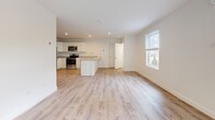 This thoughtfully designed single-floor unit offers a clean, contemporary aesthetic throughout, characterized by crisp white walls, light-toned luxury vinyl plank flooring in the main living areas, and an abundance of natural light from multiple windows. The open-concept layout seamlessly connects the kitchen and living space, creating a generous and airy atmosphere ideal for everyday living and entertaining. Sliding glass doors in the living area provide direct access to the outdoors and invite views of the surrounding greenery. The kitchen is well-appointed with white shaker-style cabinetry, light stone countertops, a central island with shiplap detailing, and a full suite of stainless steel appliances including a refrigerator, range, microwave, and dishwasher. Two bedrooms feature plush wall-to-wall carpeting and operable windows that frame views of the landscaped exterior. Each bedroom is equipped with a wall-mounted mini-split unit and baseboard heating for year-round climate control. The full bathroom is finished with light wood-look vinyl flooring, a white vanity with ample storage, a large mirror with overhead lighting, and a separate tub/shower. A dedicated utility room houses the water heater and washer/dryer hookups, adding practical convenience to this move-in ready space.