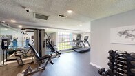 Located at 9989 Burbank Dr in Baton Rouge, LA, this fitness center offers a well-organized, single-room workout facility designed to support a full range of exercise routines. The space features durable rubber flooring throughout, a textured ceiling with recessed lighting, and large windows that allow natural light to fill the room, creating an open and energizing atmosphere.

The cardio section is equipped with multiple Matrix treadmills and elliptical machines, positioned along mirrored walls that visually expand the space and allow users to monitor their form during workouts. A multi-station cable machine serves as the centerpiece for strength training, complemented by a selection of elliptical cross-trainers and a stationary bike. The free weights area includes a full rack of dumbbells in varying sizes, medicine balls, stability balls, and foam rollers, catering to both strength and flexibility training needs.

Wall-mounted motivational artwork and signage add a purposeful aesthetic throughout the space. Ceiling fans provide additional airflow, and a mounted television offers entertainment during workouts. Security cameras are installed for safety. The gym is designed to efficiently accommodate a diverse range of fitness activities within a compact, smartly utilized footprint.