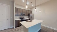 Located at 891 Ingleside Ave in Columbus, Ohio, this single-floor residence offers a thoughtfully designed layout with contemporary finishes throughout. The open-concept kitchen serves as a central highlight, featuring rich dark-stained cabinetry extending to the ceiling, white quartz countertops, a tile backsplash, and a large center island with an undermount sink. A suite of stainless steel appliances — including a side-by-side refrigerator with ice and water dispenser, electric range, and built-in microwave — completes the space. Pendant lighting with glass shades adds a refined touch above the island. The living areas are finished with durable wood-look plank flooring in a cool gray tone, while the bedrooms feature plush carpeting and windows that bring in natural light. The bathroom is well-appointed with a spacious walk-in glass-enclosed shower, a dark-stained vanity with white countertop, a framed mirror, and matching plank flooring. A dedicated laundry room houses a full-size washer and dryer alongside additional shelving for storage. The living room opens to the outdoors through a glass door, allowing natural light to fill the space and providing convenient outdoor access.
