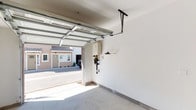 Located at 671 Woodward in San Marcos, this single-level garage offers a clean, functional layout designed to maximize utility. The space is defined by crisp white walls and a smooth concrete floor, lending a bright, well-maintained appearance throughout.

The main garage area is equipped with a sectional roll-up door featuring glass panel inserts that allow natural light to filter in when closed. An automated door opener mechanism is mounted to the ceiling track, providing convenient operation. Mounted on the interior wall is a tankless water heater alongside associated utility connections, efficiently consolidating mechanical components in one area. A standard interior access door connects the garage to the main structure, offering direct entry from the space.

A notable architectural feature is a secondary area with a vaulted ceiling and an integrated skylight, which introduces additional natural light and provides a sense of openness. This section, supported by a structural post, offers potential for storage or other uses. The overall ambiance of the garage is clean and well-lit, with views of the surrounding neighborhood visible through the open door, reflecting the residential character of the San Marcos location.