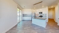 Located at 9465 W Post Rd in Las Vegas, NV, this well-appointed 2-bedroom, 2-bathroom residence offers a thoughtfully designed single-floor layout with a bright, contemporary feel throughout. The open-concept living area seamlessly connects the living room, dining space, and kitchen, all bathed in natural light from multiple windows with views of the surrounding Las Vegas landscape. The kitchen is a standout feature, boasting white shaker cabinetry, a grey subway tile backsplash, sleek quartz countertops, stainless steel appliances, and a central island with a built-in sink and pendant lighting overhead. Wood-look plank flooring flows consistently throughout the entire residence, enhancing its clean, modern aesthetic. The primary bedroom features mirrored sliding closet doors, a ceiling fan, and generous windows. A spacious walk-in closet with built-in shelving and a natural light window adds exceptional storage. The two bathrooms are finished with quartz vanities, white cabinetry, and wood-look flooring, with one featuring a walk-in glass-enclosed shower. Additional spaces include a versatile den, a dedicated laundry room, a hallway with a built-in closet, and three closets total, ensuring ample storage throughout this well-organized residence.