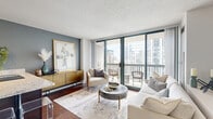 Located in the heart of Chicago's vibrant River North neighborhood at 1 West Superior Street, this well-appointed residence offers a thoughtfully designed single-floor layout. Rich hardwood flooring runs throughout, complementing the warm, contemporary aesthetic of the space.

The open-concept living and kitchen area serves as the heart of the home. The kitchen features rich dark-wood cabinetry, granite countertops, stainless steel appliances including a refrigerator and range, and a peninsula that doubles as a breakfast bar — ideal for both cooking and casual dining. The living area is bathed in natural light from floor-to-ceiling sliding glass doors that open directly onto a private balcony, offering sweeping views of the Chicago skyline and surrounding high-rises.

The bedroom is accessible via a clean, well-lit hallway and benefits from its own access to natural light through large windows. The bathroom is finished with tile flooring, a rich wood vanity with granite countertop, and a framed mirror. Additional conveniences include an in-unit laundry area and a dedicated closet for storage. The overall ambiance is modern and polished, with a neutral color palette and refined finishes throughout.