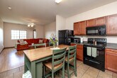 Located at 5160 Waterfront Ct in Pleasant Hill, Iowa, this one-bedroom, one-bathroom residence offers a well-designed single-level layout that maximizes every square foot of its compact footprint. The open-concept living and kitchen area forms the heart of the home, where warm hardwood flooring flows through the living room, which is brightened by multi-pane windows and finished with a ceiling fan and light fixture overhead. The kitchen is thoughtfully equipped with rich wood cabinetry, dark laminate countertops, black appliances including a refrigerator, electric range, and built-in microwave, and a tile floor that extends into the dining area. A central island with seating provides additional prep space and casual dining functionality. The spacious bedroom features plush carpeting, a ceiling fan, and a window offering natural light and outdoor views. It connects conveniently to a dedicated closet with built-in shelving, providing ample storage. The bathroom includes wood-toned vanity cabinetry, tile flooring, and access to an in-unit laundry area — a practical and highly functional feature. Throughout the residence, a neutral color palette and clean finishes create a cohesive and inviting atmosphere well-suited for everyday living.