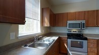 This two-story home offers a practical and comfortable layout designed for everyday living. A carpeted staircase with a clean white railing connects the two floors, providing a straightforward and functional transition between levels. The neutral-toned walls and light, airy atmosphere carry throughout the space, contributing to a welcoming ambiance.

The kitchen is a standout feature, showcasing rich warm-toned wood cabinetry that extends to the upper walls for generous storage. A double stainless steel sink sits beneath a large window dressed with horizontal blinds, allowing abundant natural light to fill the room and offer pleasant outdoor views. The kitchen is equipped with a stainless electric range and an over-the-range microwave, complemented by a tiled backsplash that adds a subtle decorative touch. Countertops provide ample workspace, making the kitchen both attractive and highly functional.

Throughout the space, the design leans toward clean lines and practical finishes, with consistent neutral wall tones that create a cohesive look across all areas. The carpeted staircase adds a soft, comfortable element to the interior, while the overall layout reflects a thoughtfully organized two-level floor plan suited to a variety of lifestyles.