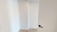 Located at 7 Fairbank Avenue West in Toronto's vibrant M6E neighbourhood, this modern one-bedroom, one-bathroom unit offers a thoughtfully designed living experience with a clean, contemporary aesthetic. The open-concept layout is anchored by striking exposed concrete ceilings and light-toned hardwood flooring throughout, creating an industrial-chic atmosphere balanced by warm, natural tones.

The spacious main living area benefits from oversized windows that flood the space with natural light while framing open city views of the surrounding Toronto neighbourhood. A sleek, integrated kitchen features charcoal grey cabinetry, stainless steel appliances, and a functional layout with track lighting above — ideal for everyday cooking and entertaining.

The generously proportioned bedroom is enclosed by full-height glass partition walls, maintaining an open, airy feel while defining the private sleeping area. Multiple windows provide abundant natural light and continued views of the cityscape. Built-in floor-to-ceiling cabinetry with glossy white finishes offers exceptional storage.

The bathroom is clean and well-appointed, featuring large-format tile flooring, a dark vanity with an undermount sink, a framed mirror, and a full soaker tub with shower. The entrance corridor connects all areas efficiently, completing a well-organized and modern unit suited for urban living.