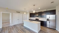 This single-floor residence showcases a thoughtfully designed open-concept layout with a seamless flow between the kitchen and living areas. The kitchen serves as the centerpiece, featuring dark espresso cabinetry extending to the ceiling for generous storage, bright white quartz countertops, and a large center island with an undermount sink and pendant lighting above. Stainless steel appliances, including a range, over-the-range microwave, and refrigerator, complete the well-equipped space.

The open living and dining areas are finished with durable wood-look plank flooring in a warm neutral tone, recessed lighting, and multiple closet storage options accessible via clean white panel doors. Natural light filters in through several windows fitted with blinds, lending the space a bright and airy feel.

The bedrooms are carpeted for comfort and each include ceiling fans and windows with outdoor views. The primary bedroom connects directly to a bathroom featuring a dual-sink vanity with quartz countertops and dark cabinetry, wood-look flooring, and a walk-in closet with built-in shelving. A secondary bathroom includes a single-sink vanity and a full tub-shower combination. Throughout, neutral warm-beige walls and consistent finishes create a cohesive, move-in-ready aesthetic.