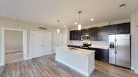 This single-floor residence showcases a thoughtfully designed open-concept layout with a seamless flow between the kitchen and living areas. The kitchen serves as the centerpiece, featuring dark espresso cabinetry extending to the ceiling for generous storage, bright white quartz countertops, and a large center island with an undermount sink and pendant lighting above. Stainless steel appliances, including a range, over-the-range microwave, and refrigerator, complete the well-equipped space.

The open living and dining areas are finished with durable wood-look plank flooring in a warm neutral tone, recessed lighting, and multiple closet storage options accessible via clean white panel doors. Natural light filters in through several windows fitted with blinds, lending the space a bright and airy feel.

The bedrooms are carpeted for comfort and each include ceiling fans and windows with outdoor views. The primary bedroom connects directly to a bathroom featuring a dual-sink vanity with quartz countertops and dark cabinetry, wood-look flooring, and a walk-in closet with built-in shelving. A secondary bathroom includes a single-sink vanity and a full tub-shower combination. Throughout, neutral warm-beige walls and consistent finishes create a cohesive, move-in-ready aesthetic.